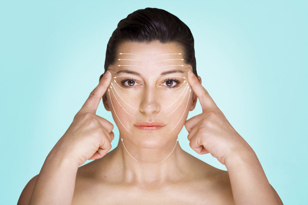 Potrait of woman stretching her face skin against blue background.
